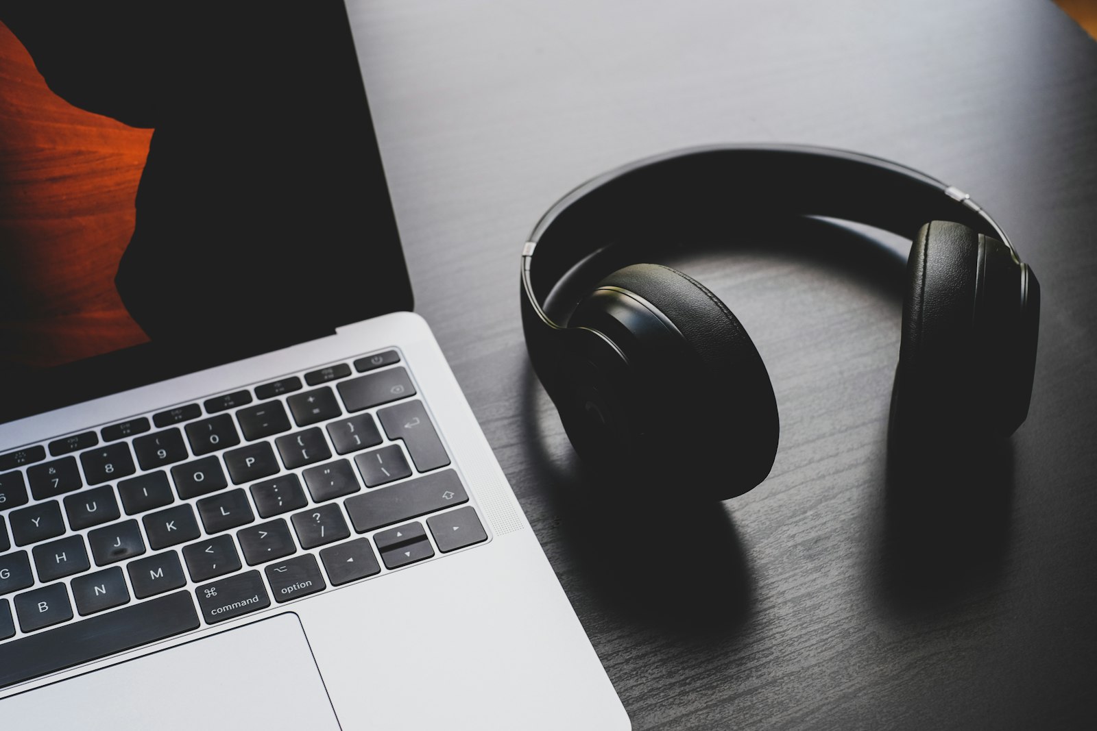 Black over-ear wireless headphones resting on a desk next to a laptop keyboard