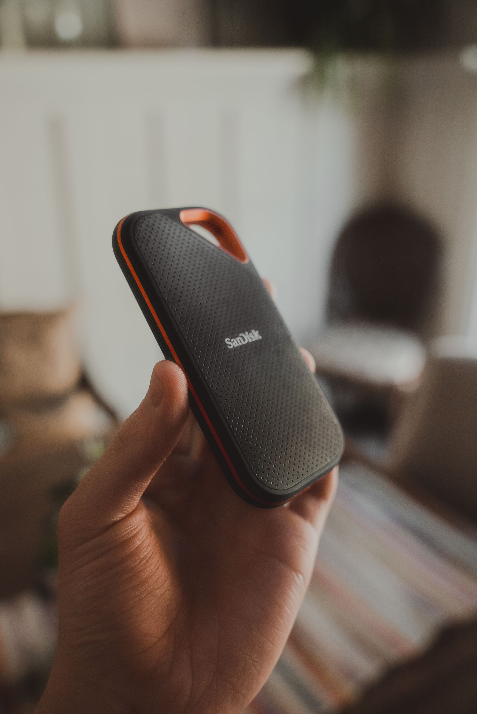 Hand holding a black and orange portable external SSD drive indoors