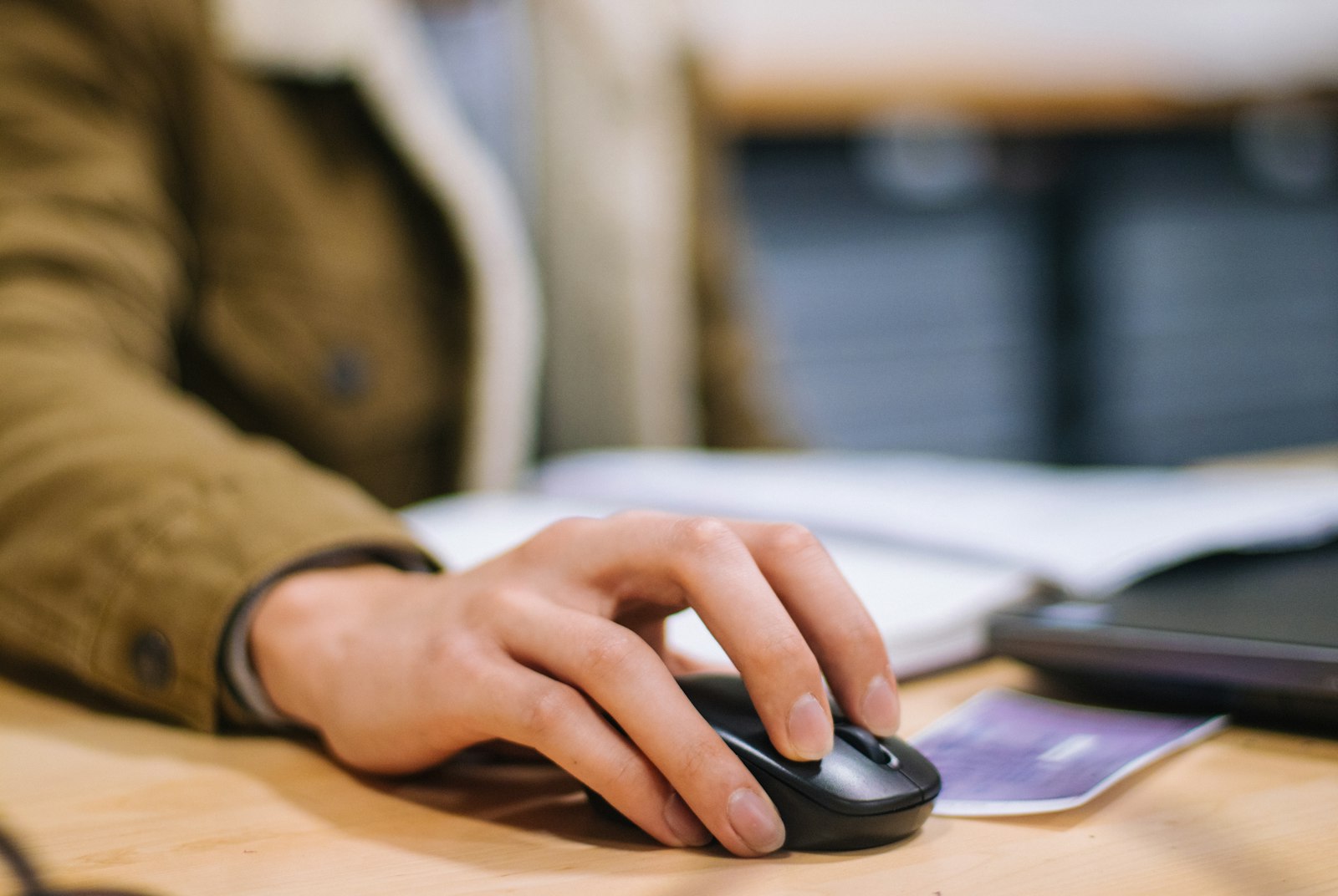 Close-up of a hand using a black wireless computer mouse on a wooden desk