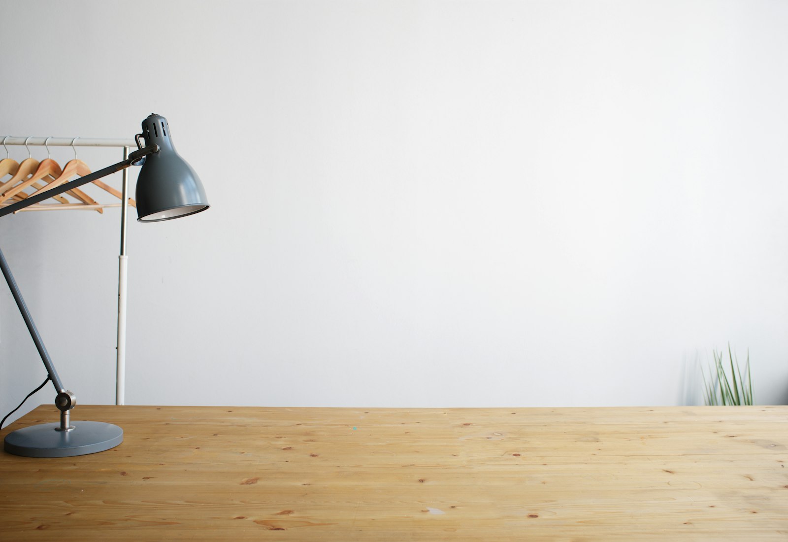 Adjustable gray desk lamp on a wooden desk against a white wall