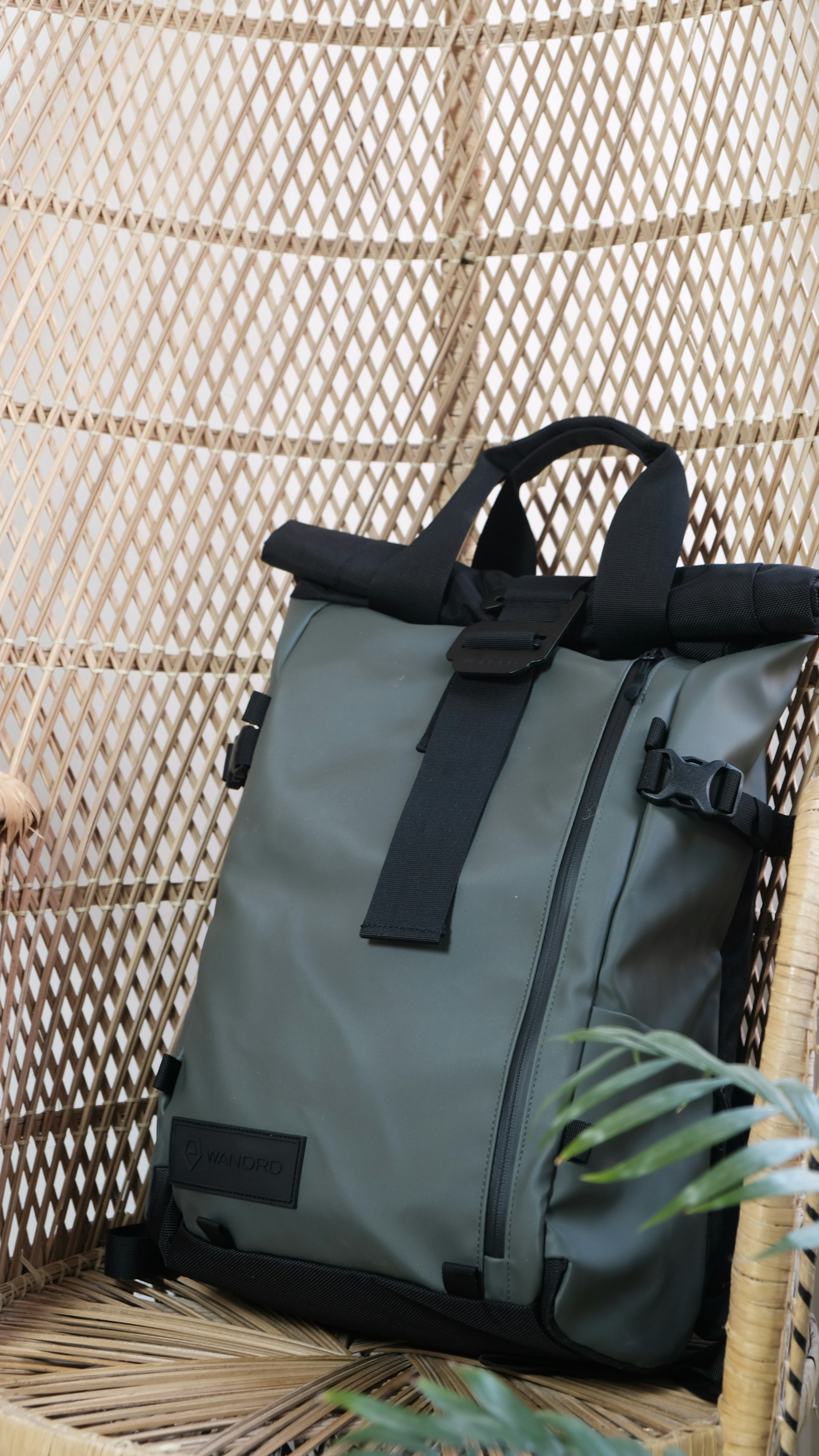 Gray rolltop backpack with buckle straps sitting on a woven chair
