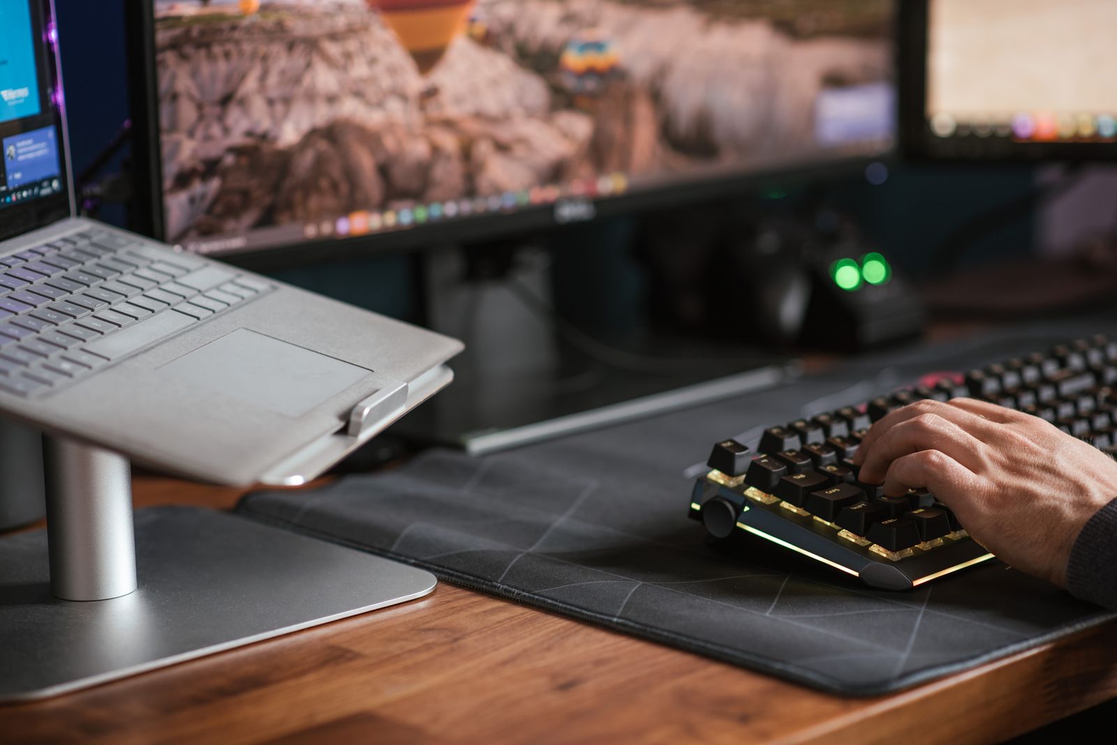 Laptop raised on a metal stand next to a hand typing on a separate external keyboard