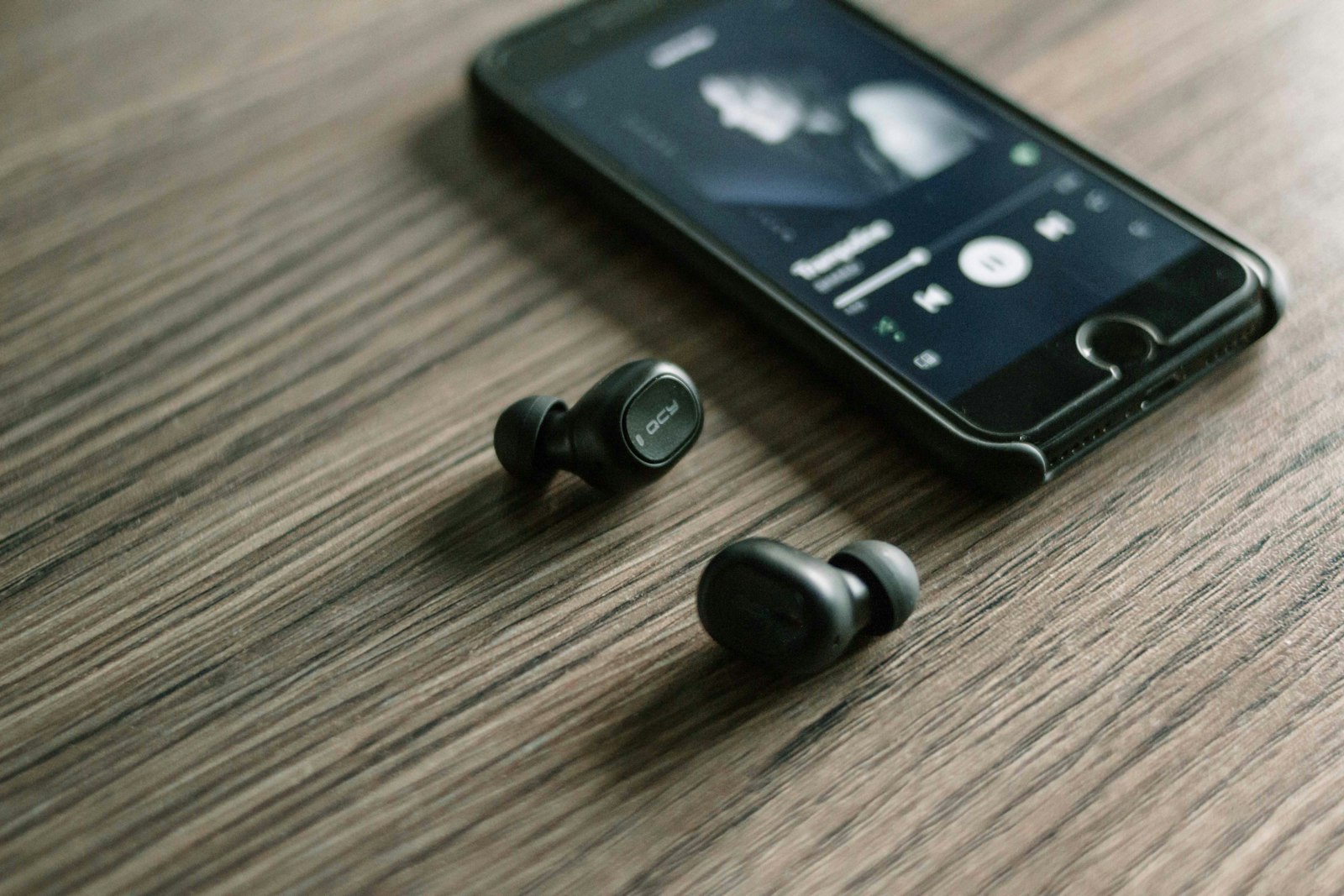 Pair of black wireless earbuds resting on a wooden table next to a smartphone