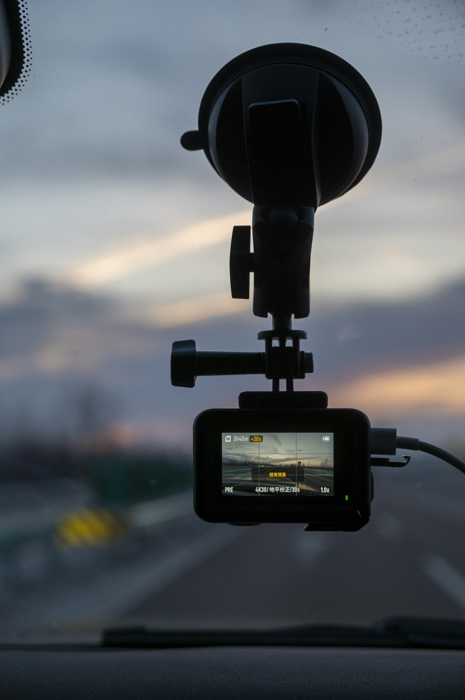 Dash cam mounted on a car windshield actively recording at sunset