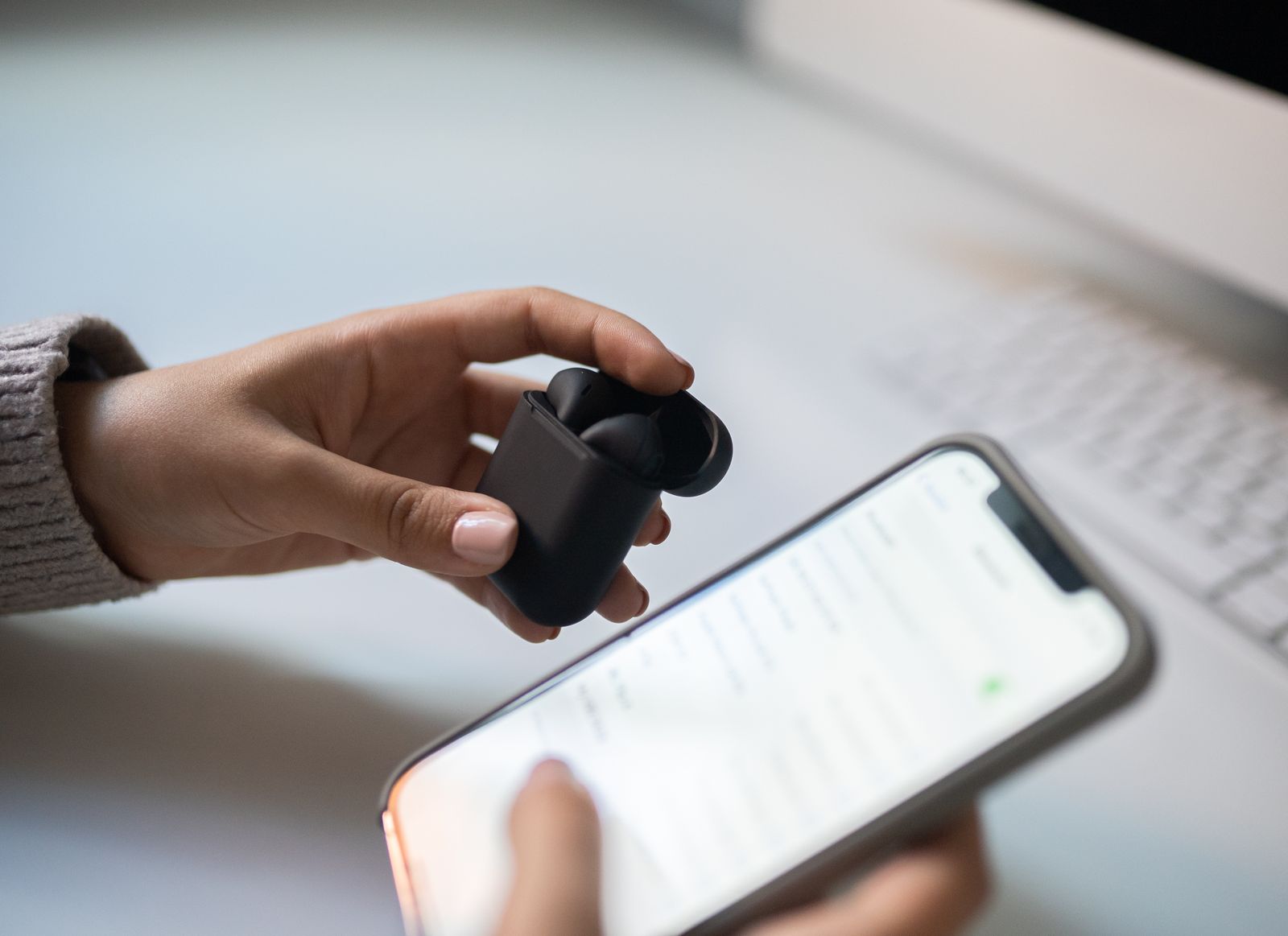 Hands holding wireless earbuds next to a smartphone
